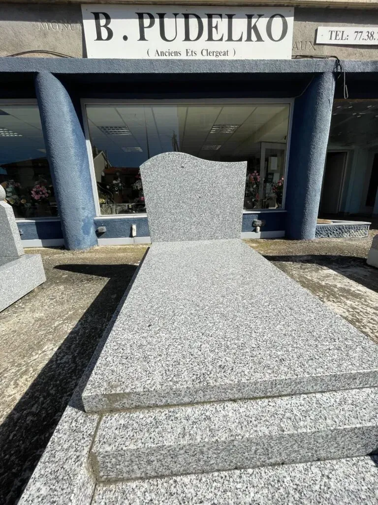 Monument funéraire en granit gris avec stèle ondulée exposé en extérieur