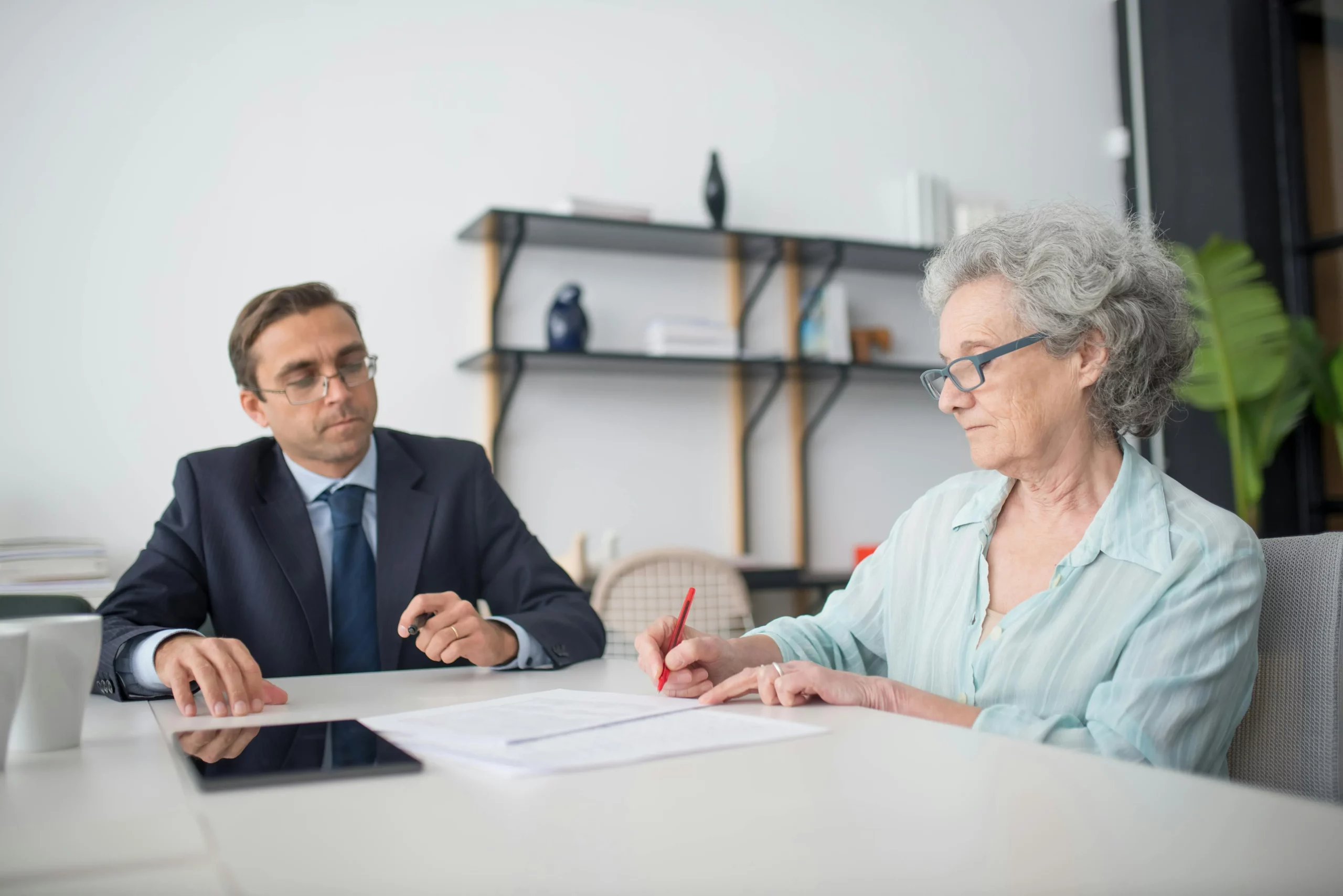 Femme senior signant un document funéraire accompagnée par un conseiller en costume